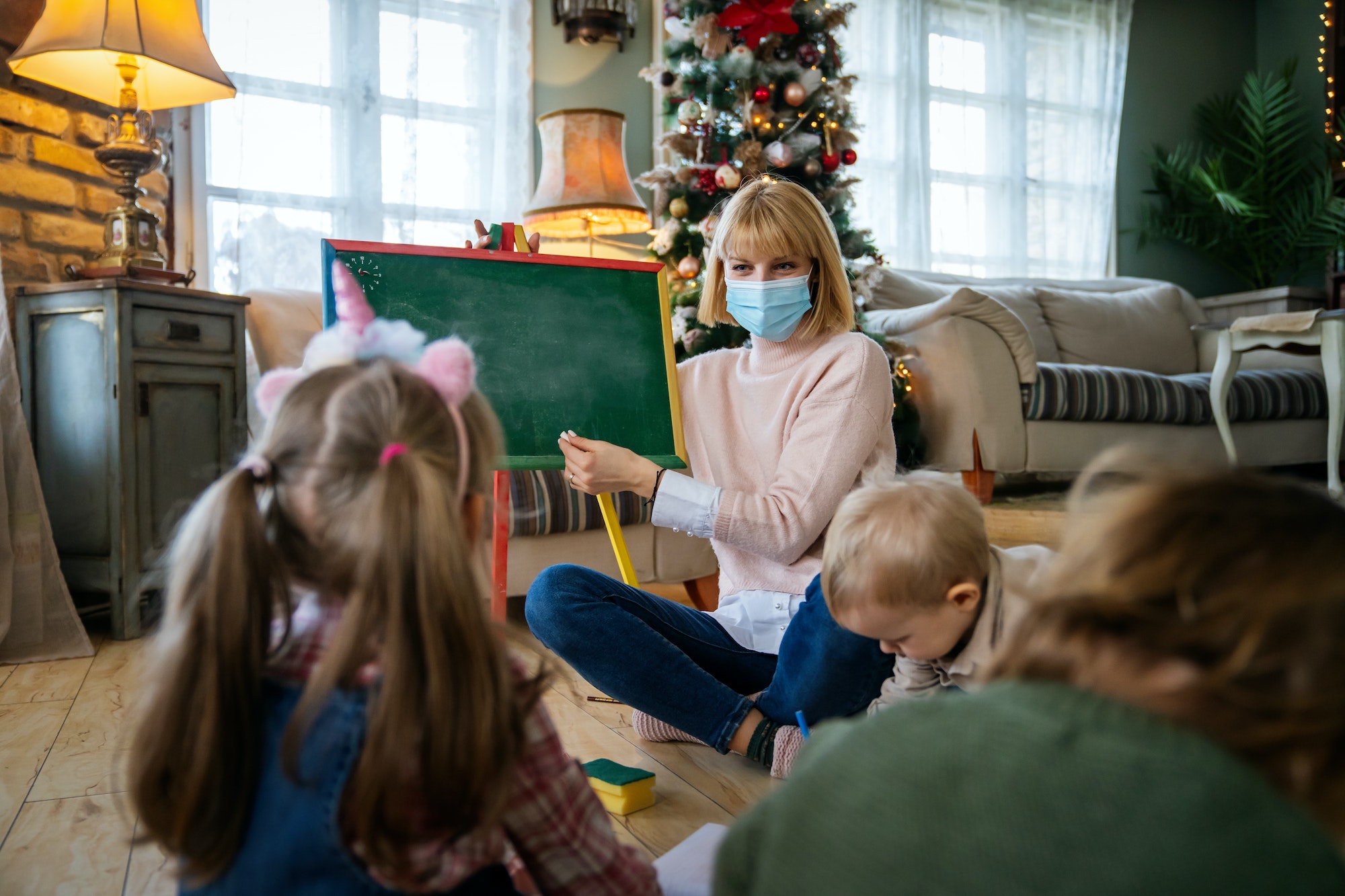 Childminder with mask and children playing together. Education, coronavirus concept